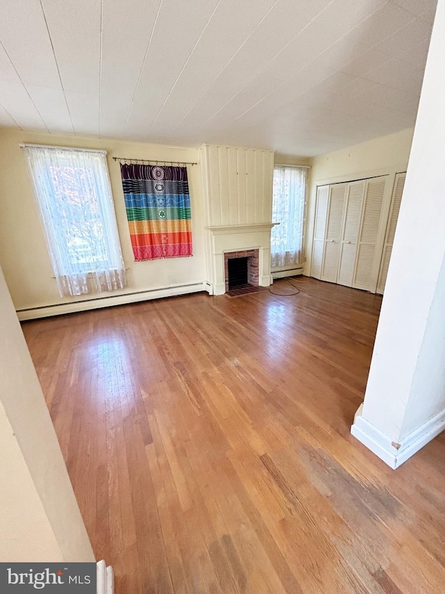unfurnished living room with a baseboard radiator, a brick fireplace, and hardwood / wood-style floors