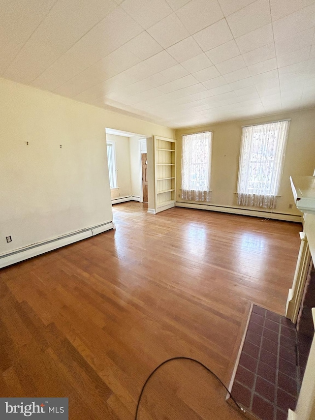 unfurnished living room with wood finished floors, a baseboard heating unit, and built in shelves