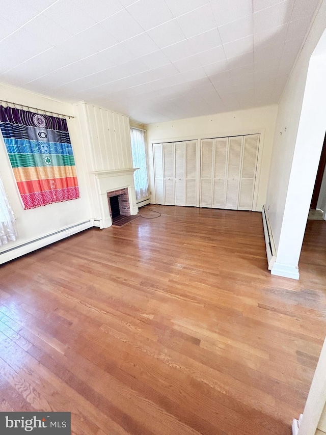 unfurnished living room with light wood-style flooring, baseboard heating, a baseboard heating unit, and a fireplace