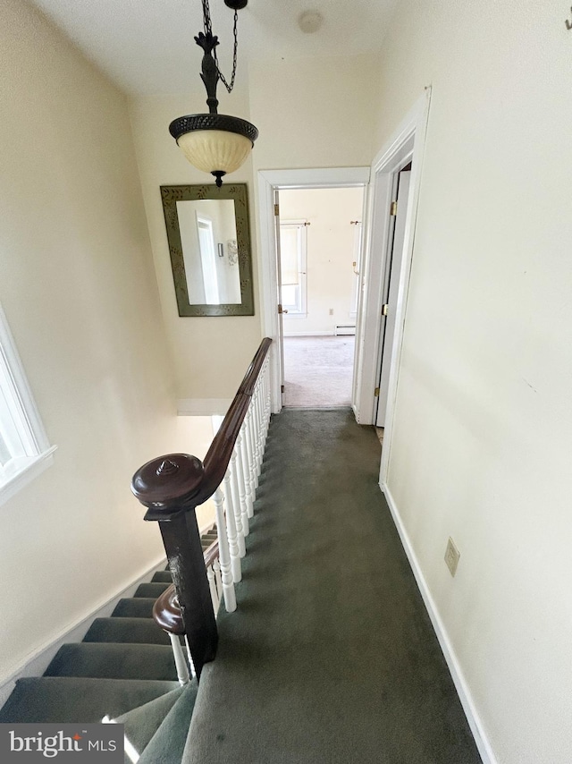 hallway with baseboards, dark colored carpet, and a baseboard heating unit