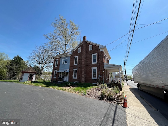 view of front of home with brick siding, an outdoor structure, a chimney, and a porch