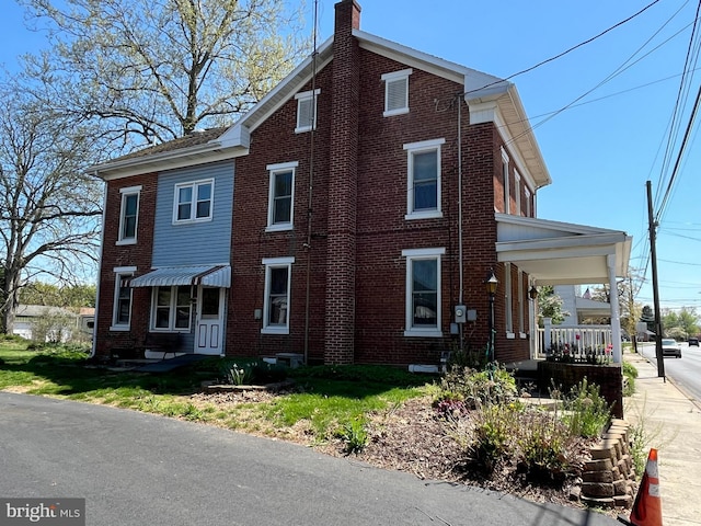 view of front of property featuring a chimney, brick siding, and covered porch