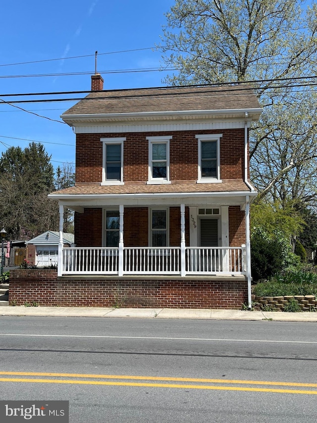 view of front facade featuring covered porch, brick siding, and a chimney