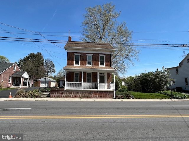 view of front facade featuring covered porch, a chimney, and brick siding