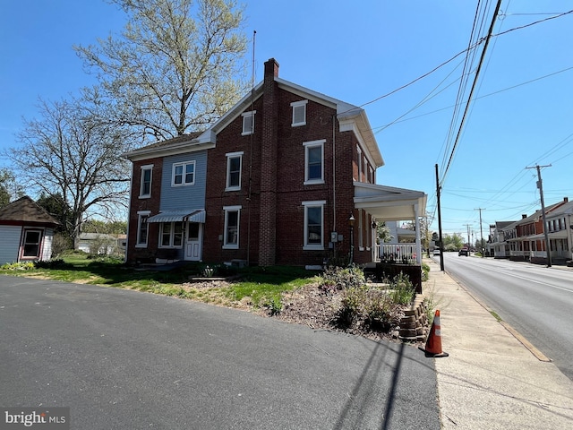 view of front facade featuring a chimney, brick siding, and covered porch