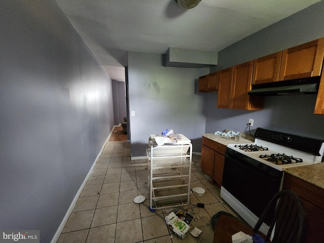 1904 Kennedy Ave, Baltimore, MD 21218 - kitchen with brown cabinetry, under cabinet range hood, gas range, light countertops, and light tile patterned floors
