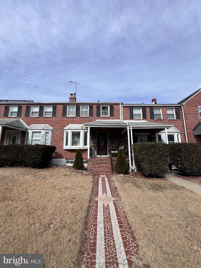townhome / multi-family property with a chimney, a front yard, and brick siding