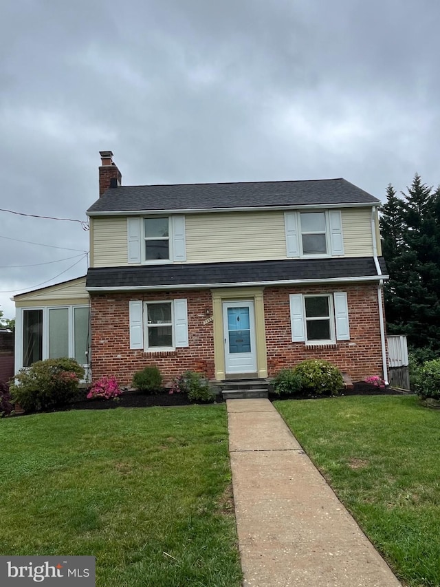 traditional home with a chimney, a front yard, and brick siding