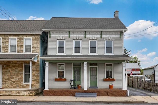 view of front facade featuring stone siding, a porch, a shingled roof, and fence