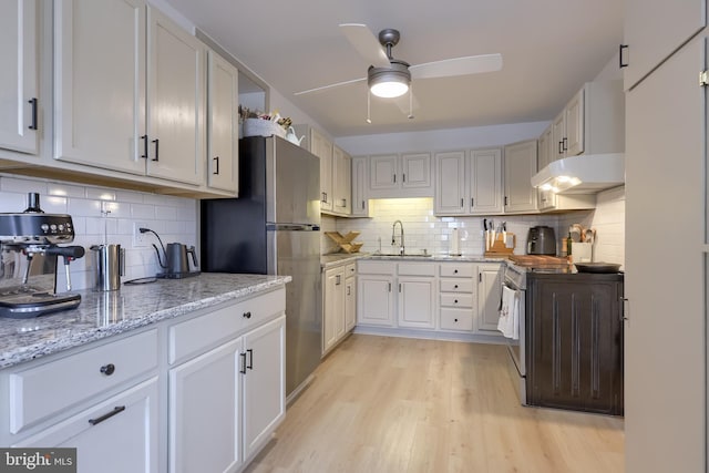 kitchen with freestanding refrigerator, a ceiling fan, under cabinet range hood, a sink, and decorative backsplash