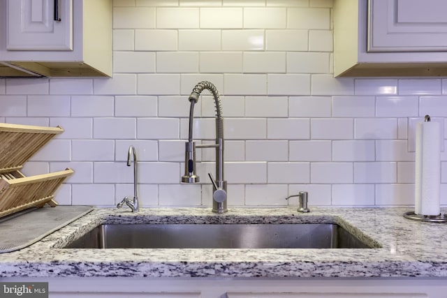 interior details featuring backsplash, light stone countertops, and a sink