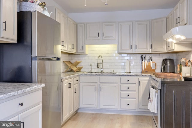 kitchen with a sink, freestanding refrigerator, range with electric cooktop, under cabinet range hood, and decorative backsplash