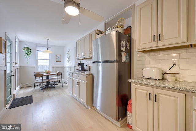kitchen featuring light wood-style flooring, a ceiling fan, freestanding refrigerator, tasteful backsplash, and light stone counters