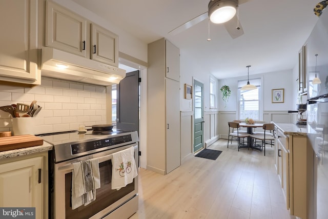 kitchen featuring light wood-style flooring, under cabinet range hood, light stone counters, stainless steel electric stove, and decorative backsplash