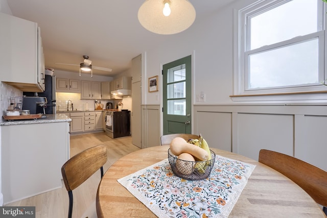 dining area with wainscoting, ceiling fan, a decorative wall, and light wood-type flooring
