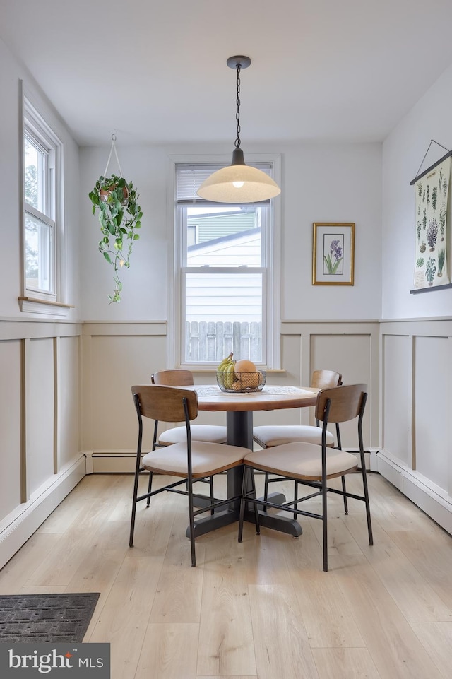 dining area featuring breakfast area, light wood-style flooring, a decorative wall, and a wainscoted wall
