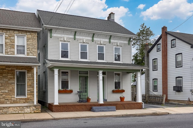 view of front facade with a chimney, stone siding, covered porch, and fence