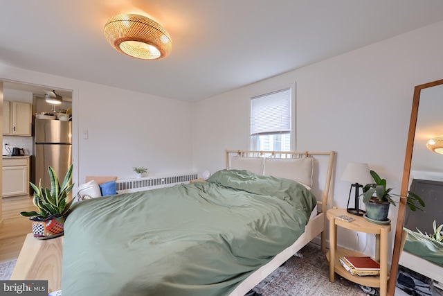 bedroom with freestanding refrigerator, radiator, and light wood-type flooring