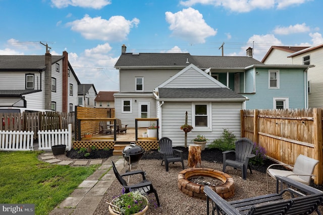 back of property with a lawn, an outdoor fire pit, a shingled roof, a deck, and a fenced backyard