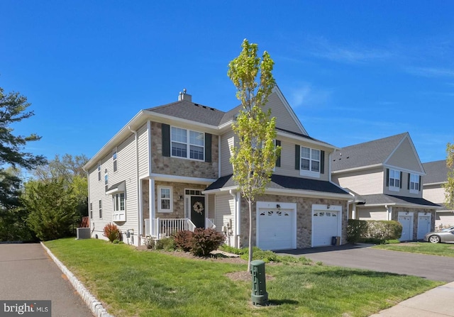 traditional-style home with a chimney, a front yard, an attached garage, stone siding, and aphalt driveway