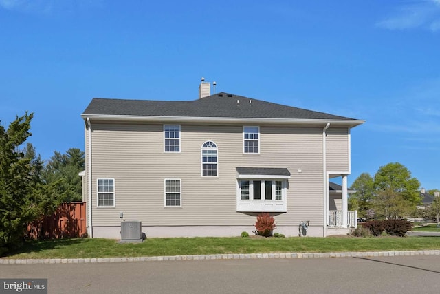 rear view of house featuring a lawn, central air condition unit, a chimney, and fence