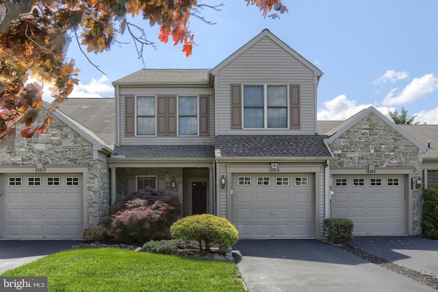 view of front of house featuring stone siding, roof with shingles, asphalt driveway, and a front yard