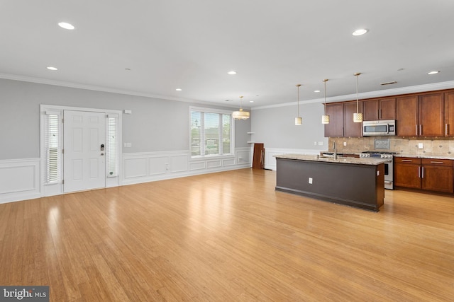 kitchen featuring stainless steel appliances, an island with sink, a sink, light wood finished floors, and decorative light fixtures