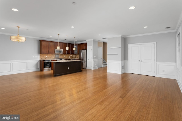 kitchen with stainless steel appliances, a decorative wall, recessed lighting, light countertops, and a kitchen island with sink
