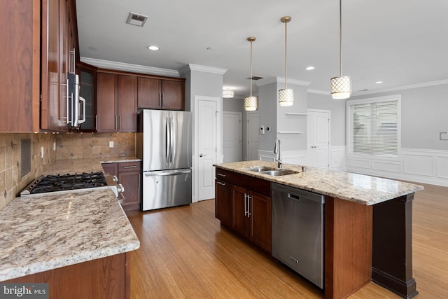 kitchen featuring stainless steel appliances, a sink, crown molding, light wood-type flooring, and decorative backsplash