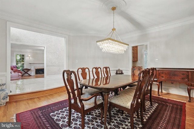 dining room with a chandelier, crown molding, wood finished floors, wainscoting, and a fireplace