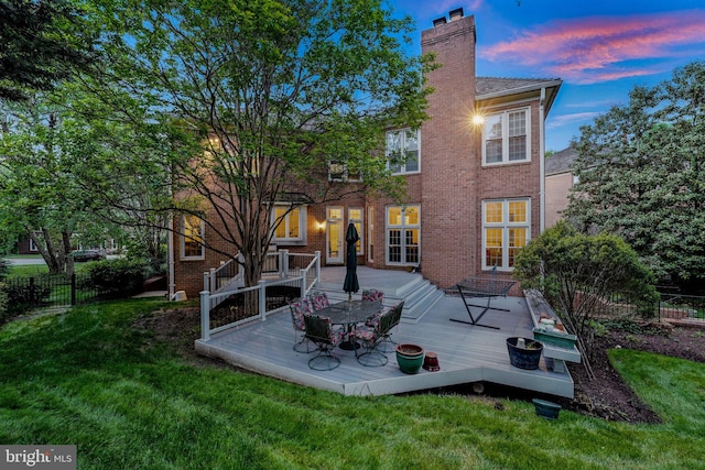 back of property at dusk featuring a deck, a chimney, and brick siding