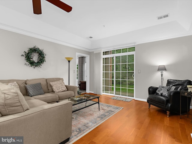 living area featuring a ceiling fan, wood finished floors, ornamental molding, baseboards, and a raised ceiling