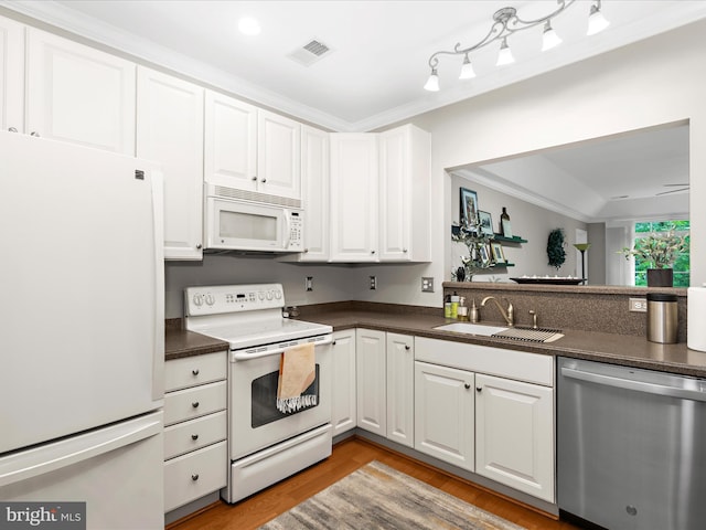 kitchen featuring white appliances, a sink, dark countertops, light wood-style flooring, and crown molding
