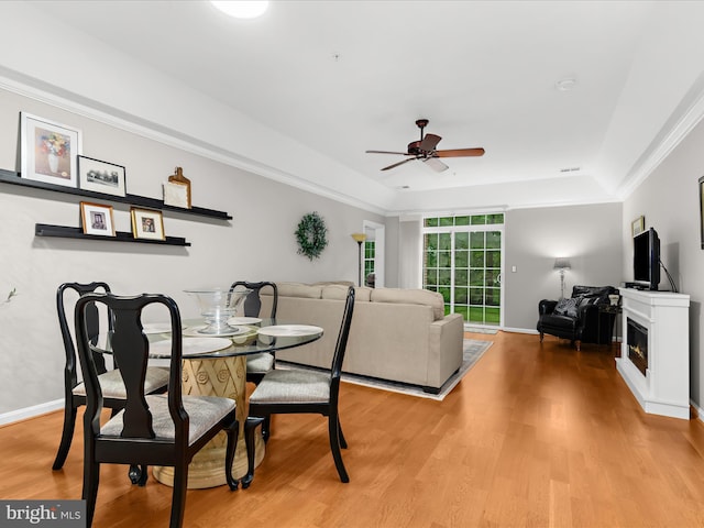 dining space featuring a ceiling fan, light wood-style flooring, a tray ceiling, baseboards, and ornamental molding
