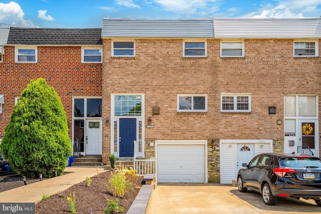 view of property with an attached garage, brick siding, driveway, and stone siding