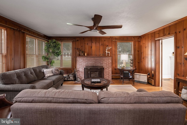 living room with wooden walls, a wealth of natural light, a ceiling fan, and a baseboard heating unit