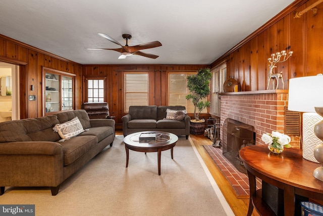living area with a ceiling fan, light wood-style flooring, wooden walls, a brick fireplace, and crown molding