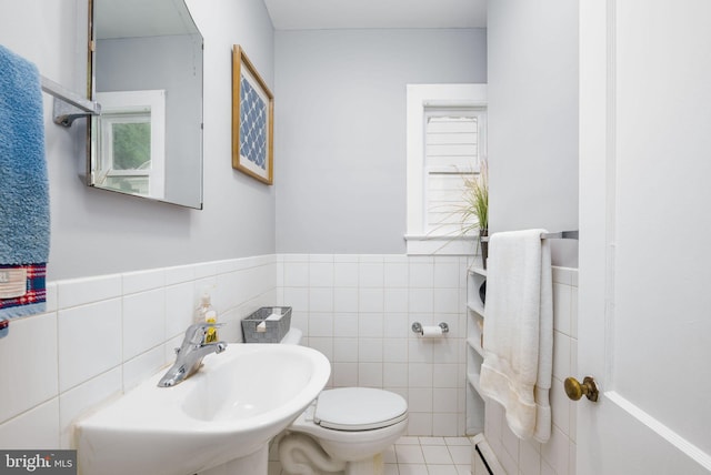 bathroom with toilet, tile walls, a wainscoted wall, and a sink