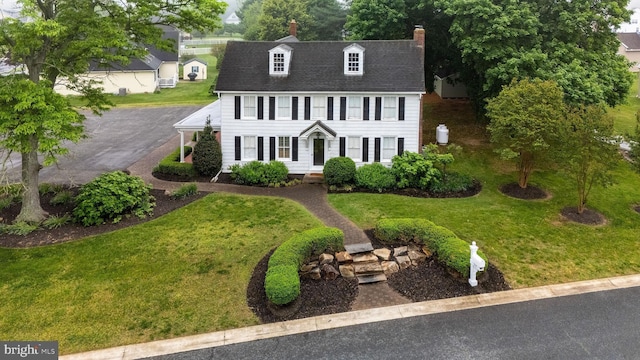 colonial house with a chimney, a front yard, and a shingled roof