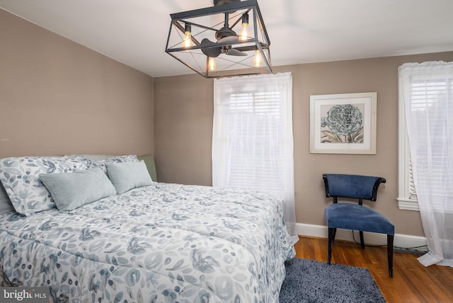 bedroom with baseboards, multiple windows, an inviting chandelier, and wood finished floors
