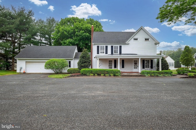 country-style home featuring a porch, driveway, a chimney, and a garage