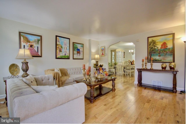 living area with arched walkways, light wood-style flooring, and a chandelier