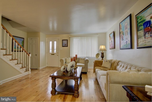 living area featuring light wood-style floors, stairway, and baseboards