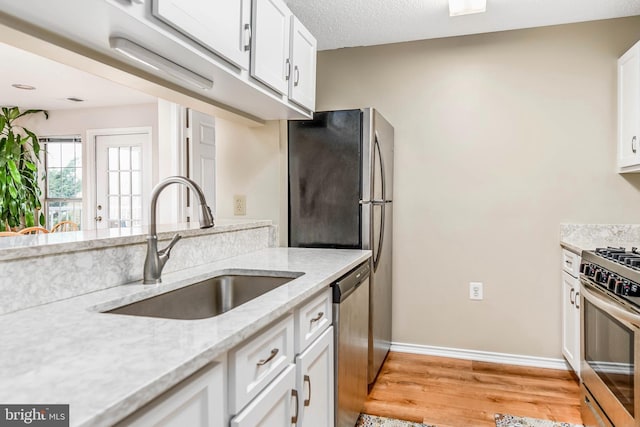 kitchen with a sink, stainless steel appliances, light wood-style flooring, and white cabinets