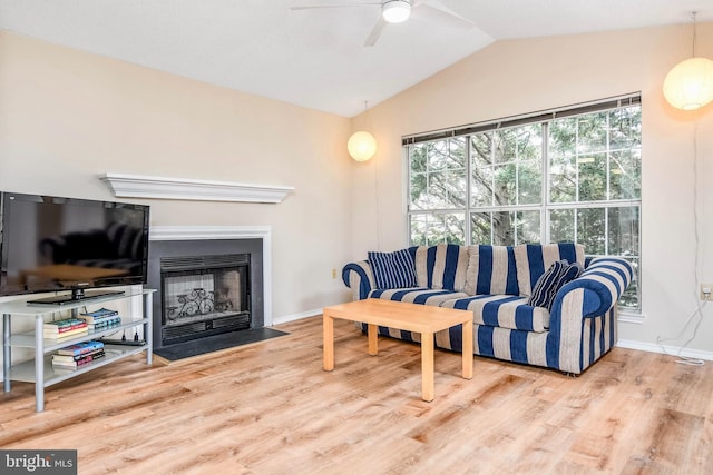 living room with lofted ceiling, ceiling fan, a fireplace with flush hearth, wood finished floors, and baseboards