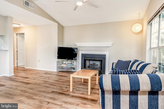 living area featuring a ceiling fan, wood finished floors, vaulted ceiling, baseboards, and a fireplace