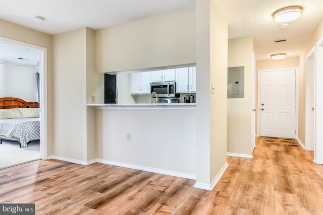 kitchen with stainless steel microwave, electric panel, and light wood finished floors