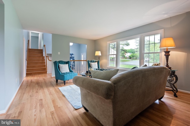 living room with plenty of natural light, light wood-style flooring, baseboards, and stairs