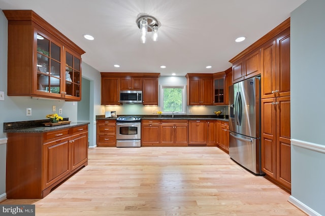 kitchen featuring glass insert cabinets, dark countertops, stainless steel appliances, light wood-type flooring, and recessed lighting