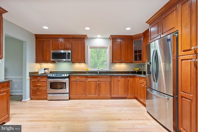 kitchen with appliances with stainless steel finishes, brown cabinetry, light wood-style flooring, and a sink